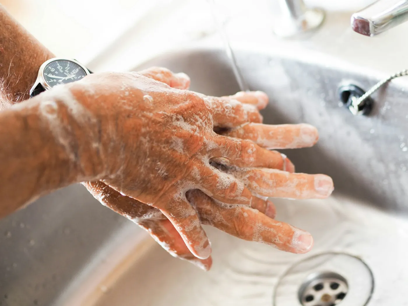 Hands being washed with soap under a running tap